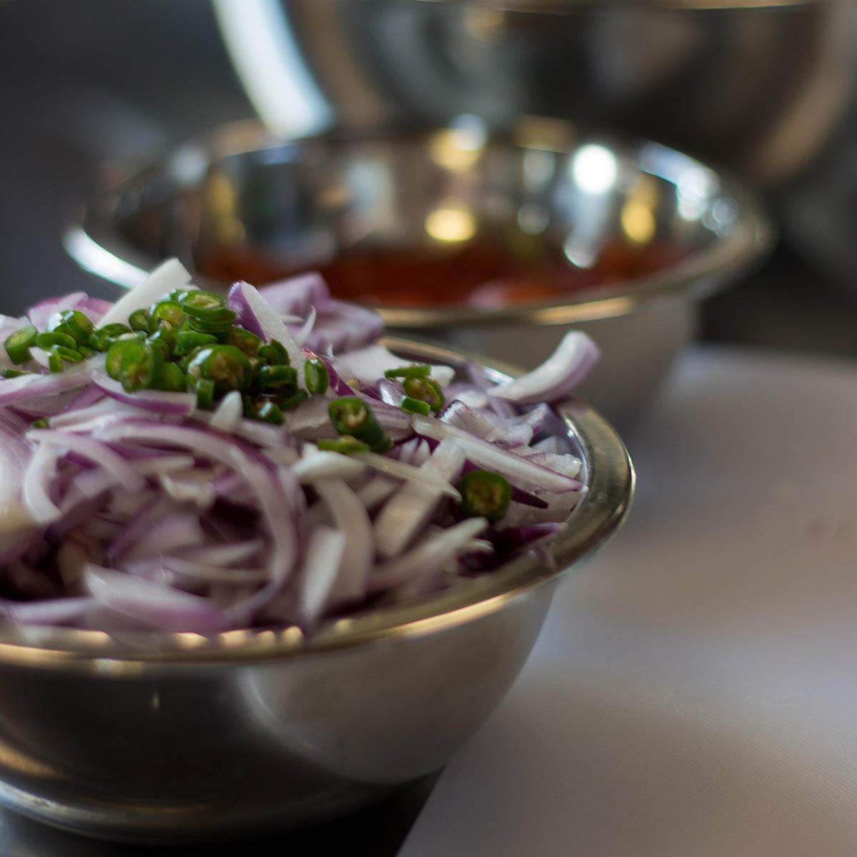 Close-up photo of chopped red onion topped with a green pepper in a silver mixing bowl