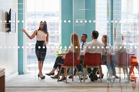 Photo of a woman in professional clothing giving a presentation in a conference room to a group of business people