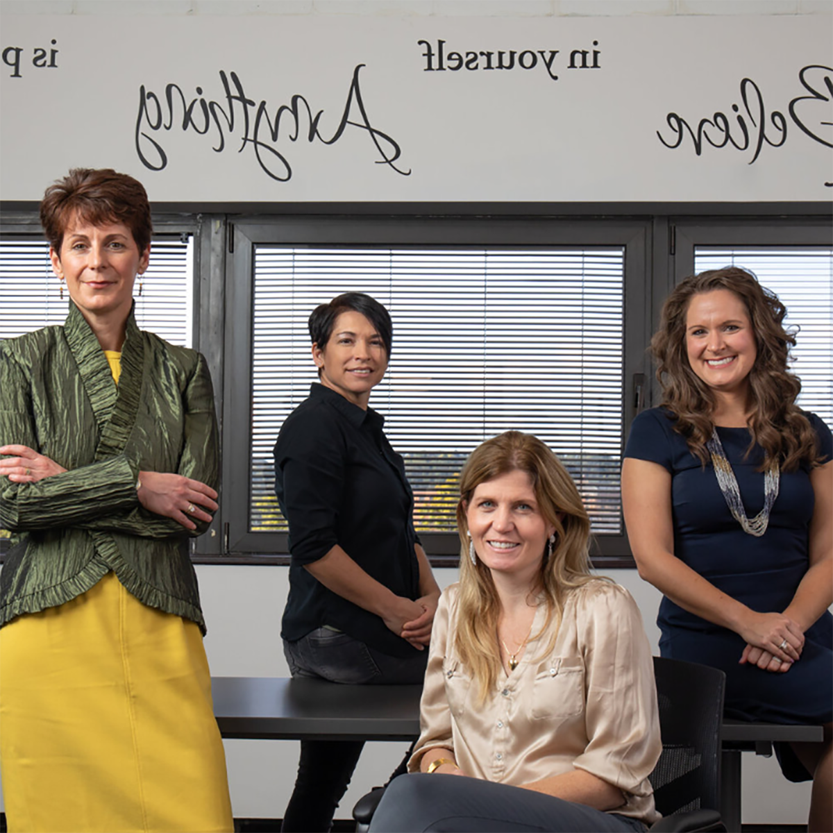 Four women in professional clothing posing for a photo in the Women's 业务 Center