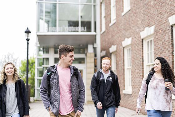 Photo of four Chatham University students leaving an academic building after class, walking and talking. 