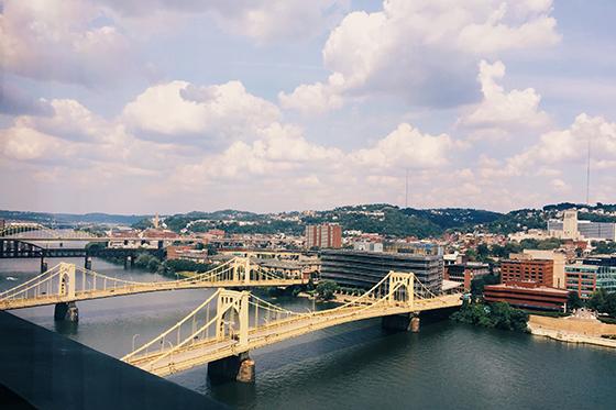 Photo of the skyline of Pittsburgh, with a river and yellow bridges