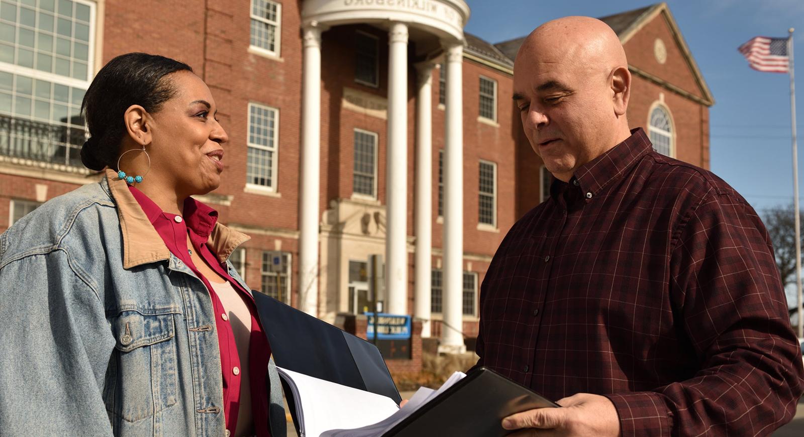 Photo of a man and woman talking outside in front of a redbrick building