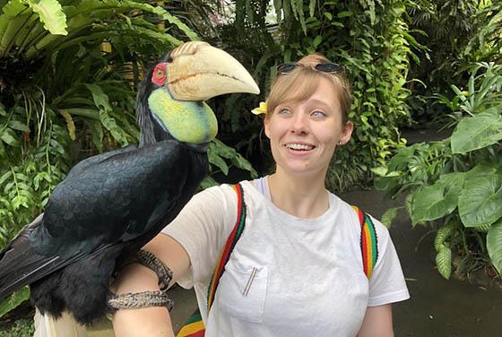 Photo of a Chatham University student in a lush rainforest with a large tropical on her arm