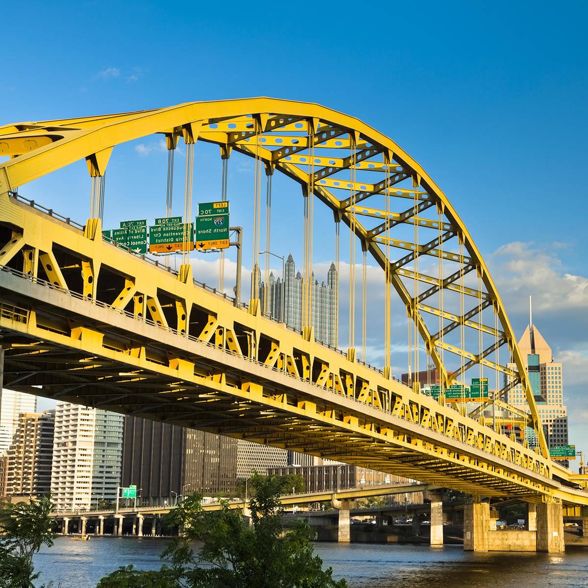 Bright photo of a yellow bridge in Pittsburgh on a sunny day against blue sky