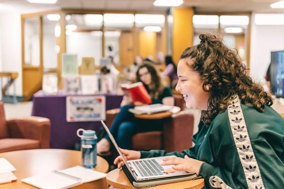 Photo of a Chatham University in the library, looking at her computer.